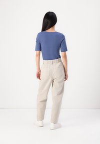 Una blusa azul de manga corta combinada con pantalones de cintura elástica beige y zapatillas blancas, fotografiada desde atrás contra un fondo sencillo.