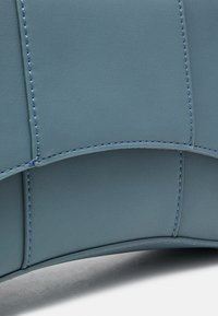 Niebieska skórzana torebka z gładką fakturą, zaokrąglonym kształtem, kontrastowym jasnym przeszyciem i widocznymi szwami.