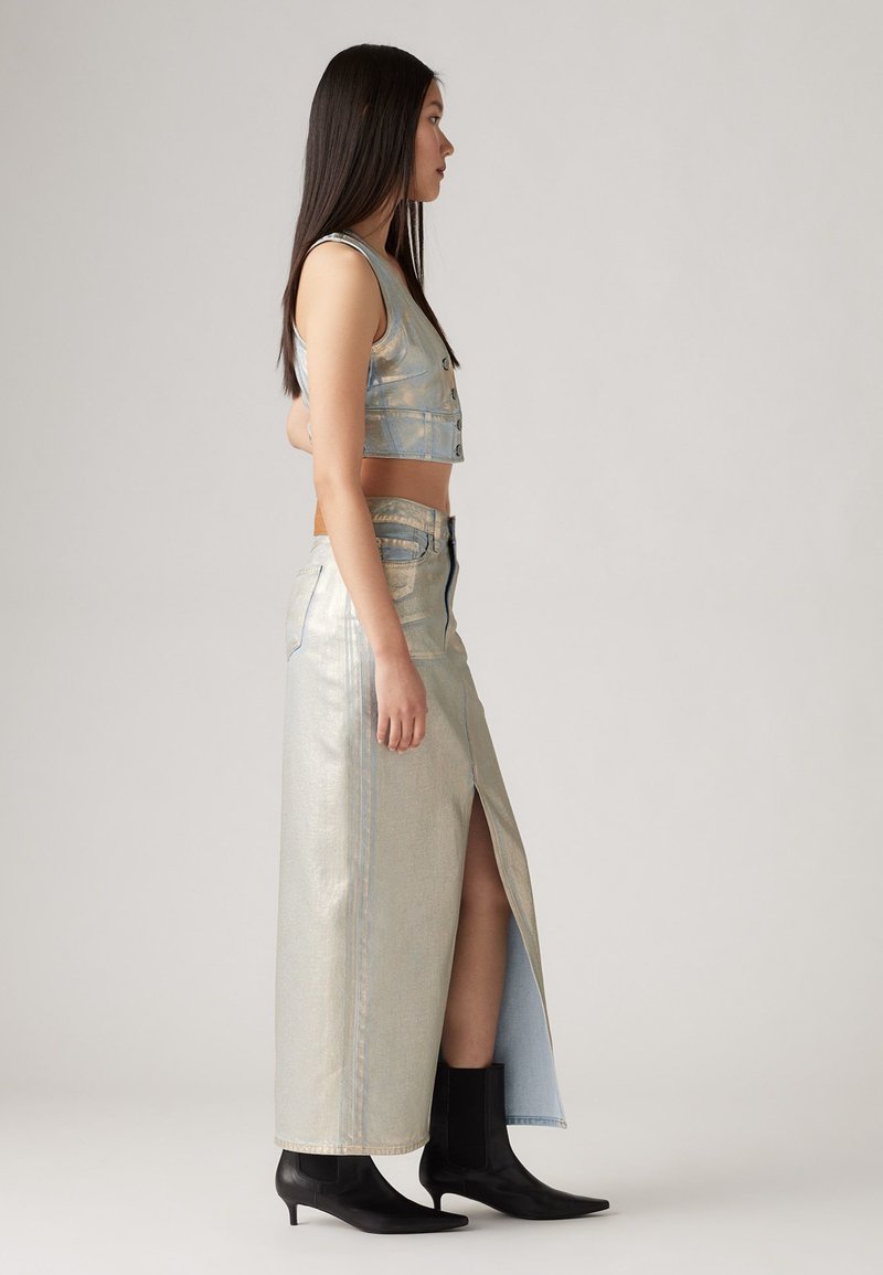 Metallic Denim-Crop-Top und langer Rock mit seitlichem Schlitz. Das Outfit hat hellblaue Töne und Nähte und wird mit schwarzen Knöchelstiefeln kombiniert.