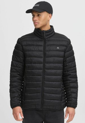 Schwarze Pufferjacke mit hohem Kragen, vertikal gestepptem Muster, Reißverschluss und seitlichen Taschen. Mit dezentem Logo auf der Brust.