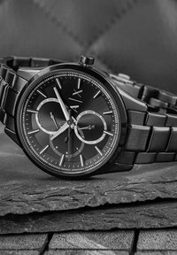 Schwarze Edelstahl-Uhr mit rundem Zifferblatt, zwei Nebenanzeigen, silbernen Akzenten und einem verlinkten Armband, auf einem Schieferhintergrund platziert.