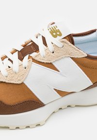 Braune Stoffsportschuhe mit weißen Akzenten und einer strukturierten beige Overlay. Ausgestattet mit flachen Schnürsenkeln und einem dezenten Logo an der Ferse. Gummisohle.