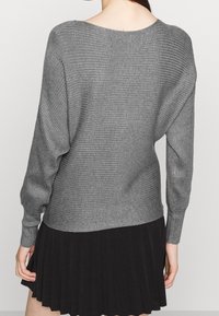 Maglione grigio a maglia con rigature orizzontali, scollatura ampia e spalle scese, abbinato a una gonna nera plissettata. Texture morbida.