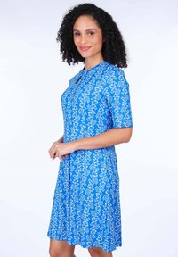 Blaues Blumenkleid mit kurzen Ärmeln, rundem Halsausschnitt und A-Linien-Schnitt. Mit einem weißen Blumenmuster auf einem einfarbig blauen Hintergrund.