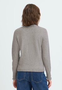 Pull en maille gris avec un col rond, des manches longues et un ourlet côtelé. Texture douce avec des coutures minimales, associé à un jean bleu.