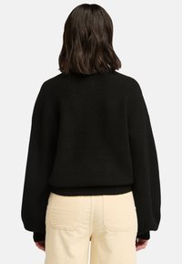 Svart stickad tröja med ribbat mönster, nedhängda axlar och avslappnad passform. Matchas med ljusgula corduroybyxor.