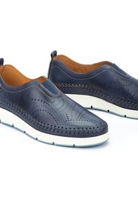 Zapatos de piel de color navy tipo slip-on con patrones perforados y suelas de goma blanca contrastante. Presenta costuras a lo largo de los lados y un interior acolchado.