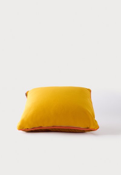 Coussin carré jaune avec tissu doux et bordure orange sur un fond clair uni.