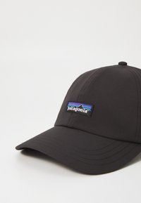 Juodas kepurė su apvaliu vainiku ir standžiu kraštu. Priekyje yra spalvingas Patagonia logotipo pleistras. Pagaminta iš lygaus audinio.