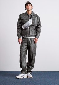 Ensemble en simili cuir gris composé d'une veste et d'un pantalon, doté de plusieurs poches. Associé à un sac en bandoulière argenté et à des chaussures de sport blanches.