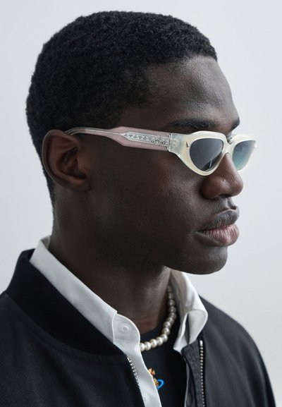 Γυαλιά ηλίου με ημιδιάφανο πλαίσιο σε ανοιχτό ροζ και λευκό, σκοτεινούς φακούς και διακοσμητικά σχέδια στα μπράτσα. Κομψός σχεδιασμός και κομψό σχήμα.