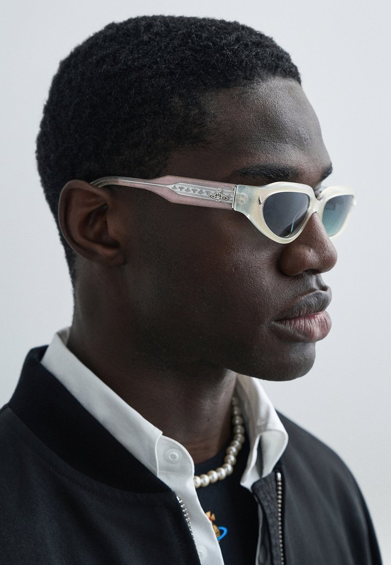 Sunglasses with a translucent light pink and white frame, dark lenses, and decorative patterns on the arms. Elegant design and sleek shape.