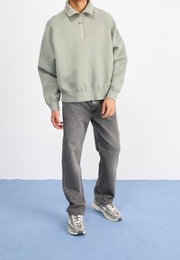 Ljusgrå sweatshirt med halvdragkedja, ribbad mudd och nederkant, tillsammans med mörkgrå raka jeans och flerfärgade sneakers.