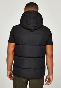 Černá vyp padded vesta s vysokým límcem, nastavitelnými popruhy a texturovanou tkaninou. Na zadní straně je vidět embosovaný text na límci.