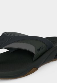 Μαύρο και σκούρο πράσινο σανδάλι τύπου slip-on με επενδεδυμένο λουράκι που φέρει το λογότυπο «REEF» και υφή καφέ σόλας.