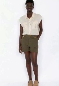 Light beige short-sleeve shirt with two chest pockets and button detail, paired with olive green high-waisted shorts featuring gold buttons.