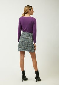 Langærmet lilla top kombineret med en tekstureret, flerfarvet tweed mini nederdel. Modellen bærer sorte ankelstøvler med en slim hæl.