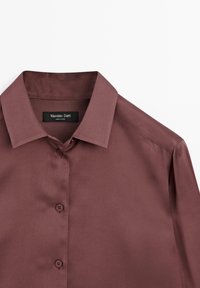 Chemise à manches longues en satin marron avec col pointu et boutons, présentée à plat avec l'étiquette de la marque "Massimo Dutti" à l'intérieur du col.