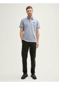 Pikétröja i ljusblått med krage, korta ärmar och en logotyp. Matchad med svarta byxor och svarta skor. Enkelt och rent design.