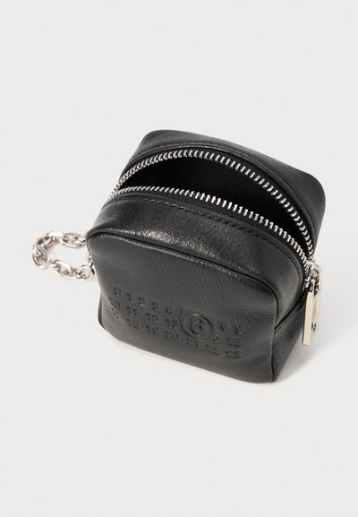 Schwarze Leder-Zippertasche mit strukturierten Oberflächen, silberner Hardware und Kettenakzent. Die Vorderseite zeigt geprägte Zahlen und ein Logo.
