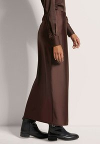 Bruine satijnen rok met een gladde textuur, met een hoge taille en een lange, vloeiende ontwerp, gecombineerd met zwarte enkellaarsjes.