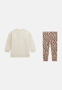 Cremefarvet langærmet sweatshirt parret med beige leggings, der har et mønster i brun og sort leopardprint samt "Guess" tekst.