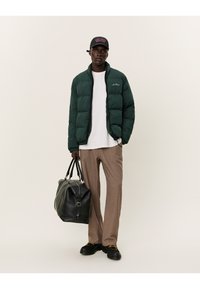 Green puffer jacket, white t-shirt, beige trousers, black shoes, and a black bag. The jacket features a zip closure and a logo detail.
