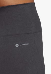 Leggings sportivi grigi scuri con un elastico a coste in vita e una superficie liscia. Presenta il logo "AEROREADY" in bianco nell'area dell'anca.