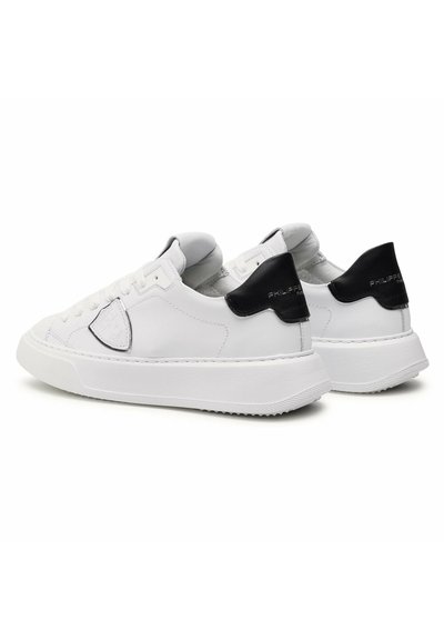 Sneaker bianche in pelle con accenti neri, con punta arrotondata, chiusura con lacci e un pannello testurizzato sul lato. Suola in gomma piatta.