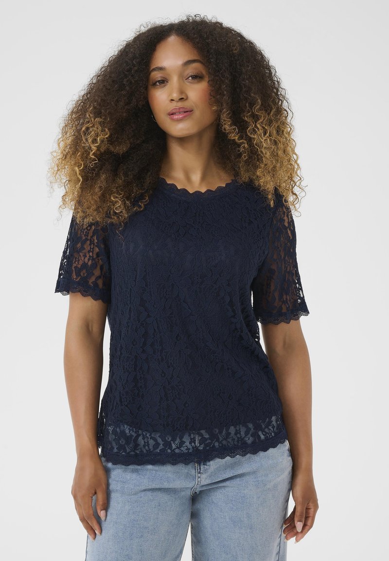 Top in pizzo blu navy con maniche corte a scallop, intricate fantasie floreali e scollo scallop. Presenta un design testurizzato e a strati.
