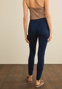 Tummansinisiä slim fit -farkkuja, joissa on kaksi takataskua ja korkea vyötärö. Kangas on sileä.
