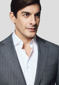 Szary garnitur w prążki z białą koszulą. Zbliżenie na twarz mężczyzny, prezentujące gładką skórę i krótkie, ciemne włosy.