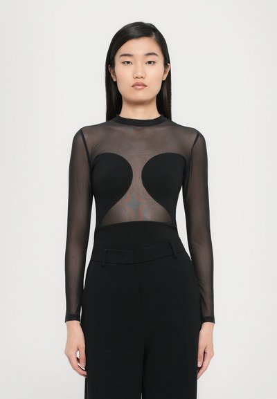 Haut noir à manches longues avec un design en maille transparente, présentant une découpe en forme de cœur au niveau de la poitrine, associé à un pantalon noir taille haute.