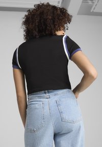 Camiseta corta negra con mangas cortas, que cuenta con acentos en azul y blanco en los puños, combinada con jeans de tiro alto en un azul claro.