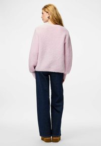 Vaaleanpunainen neulottu rento neulepaita, jossa pyöreä pääntie ja resorit hihansuissa, yhdistetty tummansinisiin leveälahkeisiin farkkuihin ja ruskeisiin korotettuihin kenkiin.