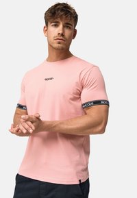 Tricou din bumbac roz cu mâneci scurte, cu dungi negre și logo pe mâneci. Croială moderată și textură netedă.