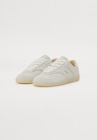 Sneakers in suede grigio chiaro con lacci bianchi e suola in gomma. Presentano borchie decorative sul lato esterno e un colletto imbottito.