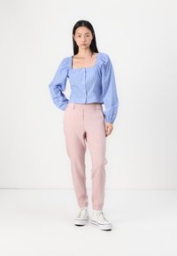 Lys blå stripete bluse med kvadratisk hals og puffermer; kombinert med rosa skræddersydde bukser og hvite høyhælte sneakers.
