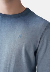 Heller blauer Strickpullover mit einem gerippten Rundhalsausschnitt. Verfügt über einen subtilen Farbverlauf und ein gesticktes Logo auf der Brust. Weiche Textur.