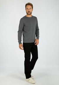 Maglione grigio lavorato a maglia con orlo a coste, abbinato a pantaloni neri e sneaker crema. Il look presenta un design casual e una silhouette aderente.