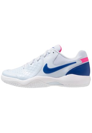 Chaussure de sport blanche avec logo Nike bleu, accent rose au talon et semelle texturée conçue pour le sport ou un usage décontracté.