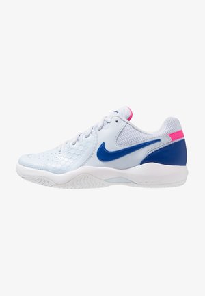 Chaussure de sport blanche avec logo Nike bleu, accent rose au talon et semelle texturée conçue pour le sport ou un usage décontracté.