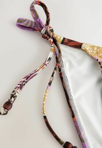 Costum de baie cu un top cu bretele colorate, cu un detaliu legat, din material alb în contrast și cusături decorative pe margine.
