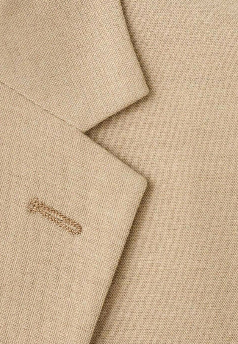Beige blazer detail featuring textured fabric, with a visible stitching accent on the lapel and a smooth, tailored silhouette.