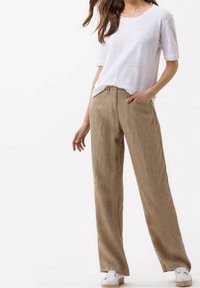 Pantalon léger en lin beige à coupe décontractée, poches latérales et taille à cordon, associé à un haut blanc à manches courtes et des baskets.