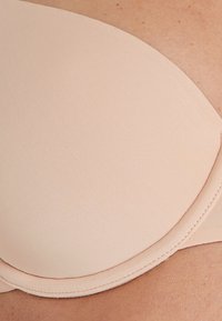 Reggiseno imbottito rosa chiaro con una texture liscia e a coste e bordi senza cuciture. Presenta coppe rotonde e un design leggermente strutturato.