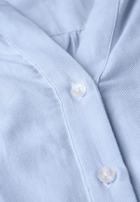 Camicia azzurro chiaro in tessuto con colletto, dotata di una linea di bottoni bianchi e un delicato motivo intrecciato.