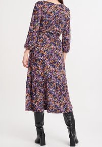Květinové midi šaty v tmavě fialové barvě s oranžovými a žlutými akcenty. Dlouhé rukávy, páskový pas a vrstvený lem. Nosit s vysokými černými botami.