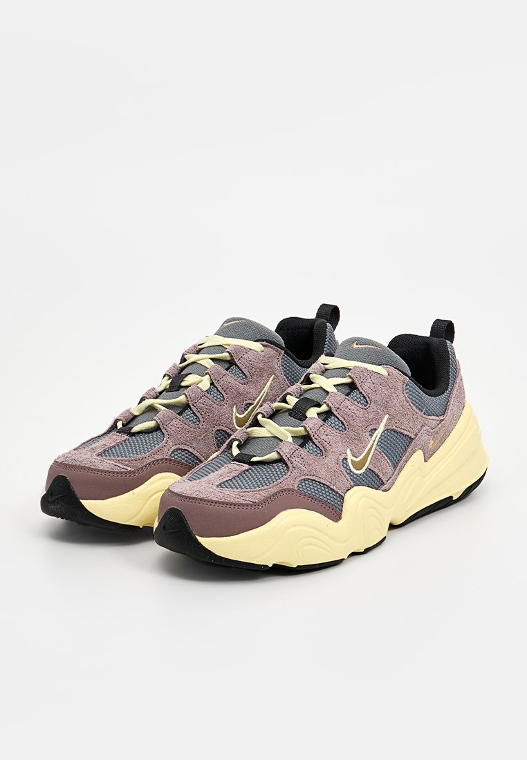 Sneakers Nike z cholewką wykonaną z mieszanych materiałów w kolorach purpurowym, szarym i żółtym. Posiadają teksturowaną powierzchnię, sznurowaną konstrukcję oraz czarną gumową podeszwę.