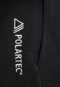 Black fleece fabric with a textured surface, featuring a white embroidered logo that includes a triangle and the word "POLARTEC."
